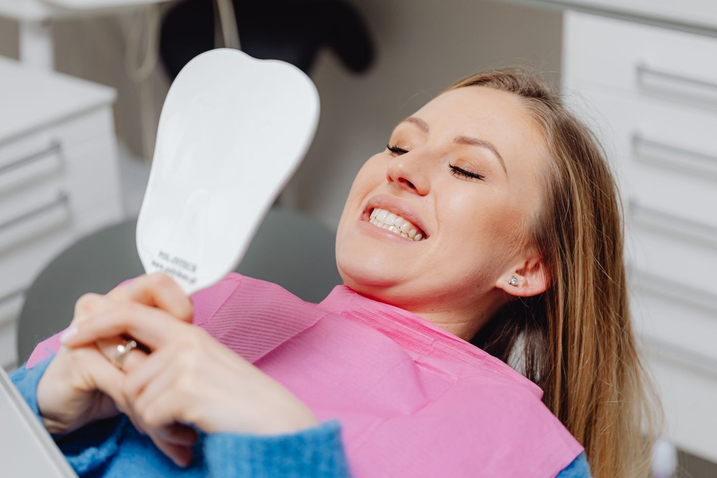 Paciente sorrindo, olhando o próprio sorriso no espelho após atendimento